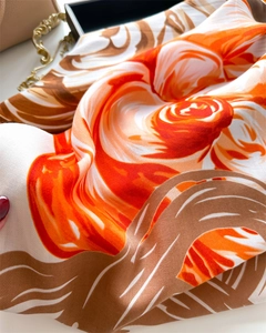 Close-up of elegant twill silk scarf showing detailed orange floral pattern and soft texture