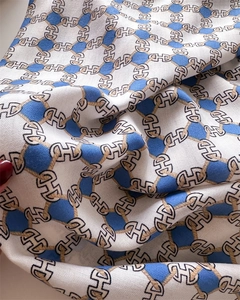 Dettaglio foulard in seta di lusso con motivo a catena dorata e stampa monogramma H