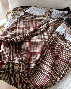 Detailed close-up of plaid silk scarf fabric with golden chain and horsebit patterns