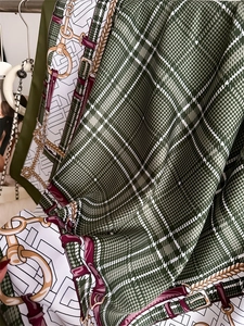 Detail of silk-like scarf featuring green plaid patterns with equestrian gold chain prints