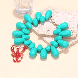 Detail of turquoise water-drop beads and red lobster pendant on a golden chain necklace