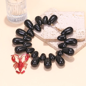 Detailed macro of vibrant red enamel lobster pendant on polished black beaded necklace