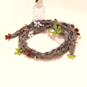Long braided fabric necklace with colorful resin flowers and gold beads on beige background