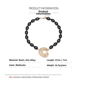 Détail du pendentif en C texturé avec des perles en résine noire sur collier doré