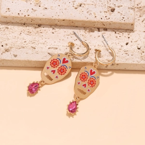 Detail van schedel oorbellen met rode bloemen, roze stenen en gouden finish