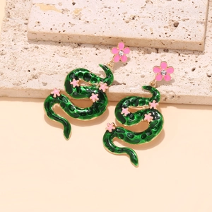 Close-up of green enamel snake earrings with pink flowers and crystal studs on stone
