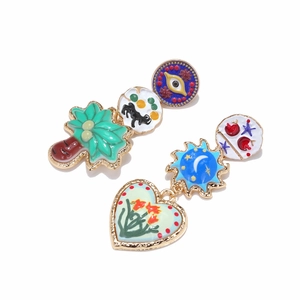 Macro detail of asymmetric alloy drop earrings with palm tree, eye, and heart charms