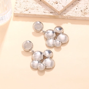 Close-up of tiered polished silver round bubble earrings on a warm beige background