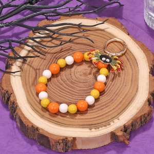 Detail of Halloween beaded charm featuring a colorful enamel spider pendant on wood