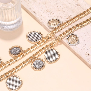Détail de pendentifs géométriques bicolores sur un collier à grosse chaîne dorée