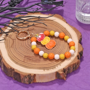 Halloween beaded keychain with orange pumpkin pendant on a rustic wood slice background