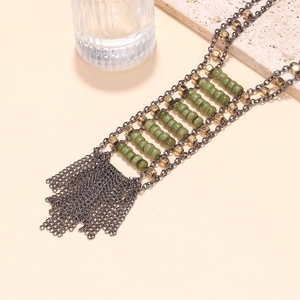 Macro detail of Bohemian layered metal chain necklace with green beads and fringe tassels