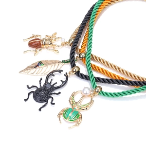 Détail de pendentifs scarabée et feuille colorés sur cordons tressés en émail