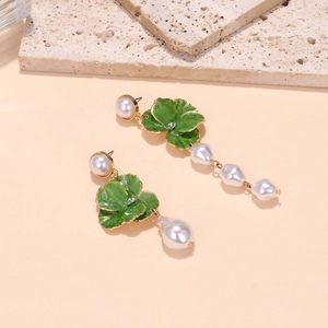 Detail of asymmetrical baroque pearl earrings with green enamel flowers and gold base