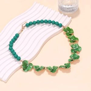 Détail du collier fleur en émail avec perles vertes sur un support ondulé blanc