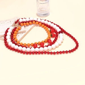 Close-up of layered beaded necklaces with red strawberry charms and golden clasp
