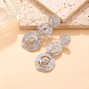 Close-up of tiered silver spiral drop earrings with brushed metal texture on stone surface