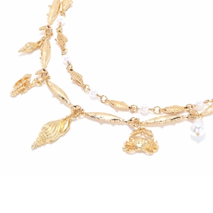 Detailed close-up of golden sea shell, fish, and crab pendants with pearls on a layered necklace