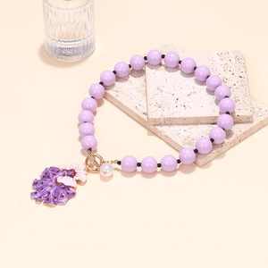 Detail of purple beaded bracelet with flower charm and golden toggle clasp on stone