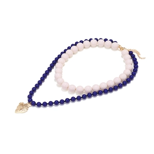 Dettaglio di collana a strati con perle blu e crema e ciondolo dorato a forma di anfora antica