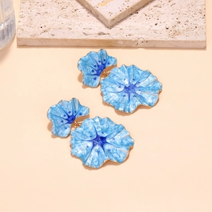 Detailed close-up of blue enamel flower earrings with golden edges on travertine stone