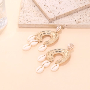 Detail of bohemian gold C-shape earrings with white pearls and hanging sea shells