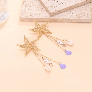 Detail of golden starfish earrings with seahorse and purple shell tassels on stone