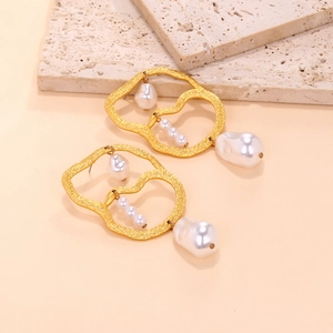 Detail of golden textured geometric earrings with baroque pearls on travertine stone