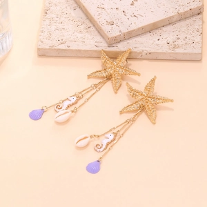 Detail of gold starfish earrings with white seahorse and seashell charms on stone