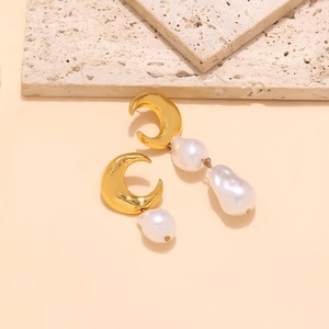 Detailed view of asymmetric crescent moon and baroque pearl drop earrings on stone