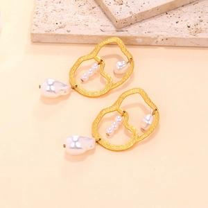 Detailed macro of golden irregular hoop earrings with baroque pearls on stone decor