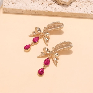 Detail of elegant gold feather earrings with pink pear-shaped gemstones and ribbon bow