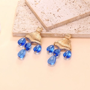 Detail of vintage gold fan studs with navy blue teardrop beads on a textured stone surface