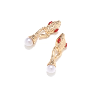 Macro detail of gold snake earrings with red rhinestone eyes and white faux pearl