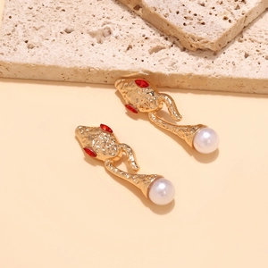 Golden snake earrings with red gemstone eyes and white pearls on natural stone