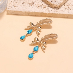 Detail of gold bow earrings with feather texture and blue crystal teardrop pendants