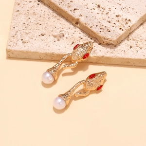 Detailed view of snake head earrings with red gem eyes and white pearls on stone