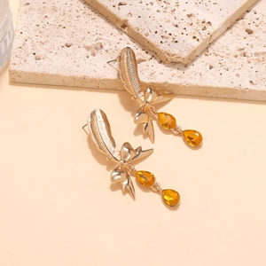 Detailed close-up of golden feather earrings with ribbon bow and amber teardrop gems