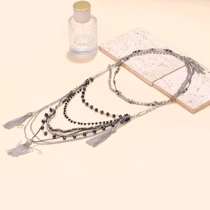 Detail of beaded waterfall fringe necklace with multi-layer chains on a beige stone surface