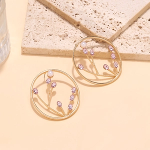 Macro shot of gold floral hoop earrings with pink gemstones and pearls on a stone