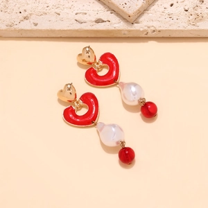 Detail of baroque pearl drop earrings with red enamel hearts and golden metal accents