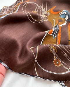 Macro detail of silk scarf showing herringbone texture, bridle prints, and fine edging