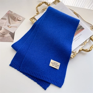 Écharpe en tricot bleu roi avec bords côtelés et étiquette, posée sur plateau doré