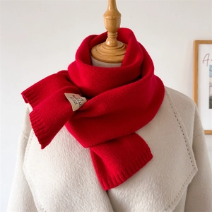 Détail d'une écharpe en maille rouge avec étiquette tissée sur un manteau crème