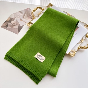 Détail d'une écharpe en maille verte avec étiquette vintage sur plateau doré