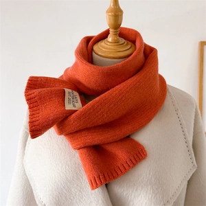 Détail de la texture d'une écharpe en maille orange avec étiquette vintage sur manteau