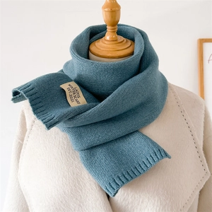 Détail de l'écharpe en tricot bleu avec étiquette sur un manteau en laine beige
