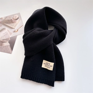 Détail d'une écharpe en maille noire avec une étiquette tissée blanche et texte sur fond épuré