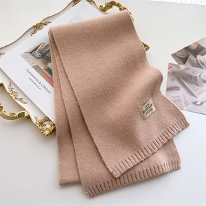 Détail d'une écharpe en maille camel clair avec étiquette hiver et bordure côtelée
