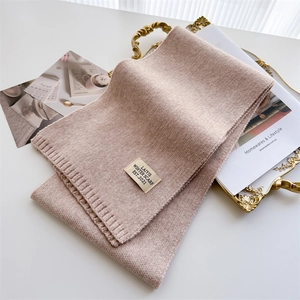 Détail de l'écharpe en maille rose avec écusson minimaliste et bordure en côtes